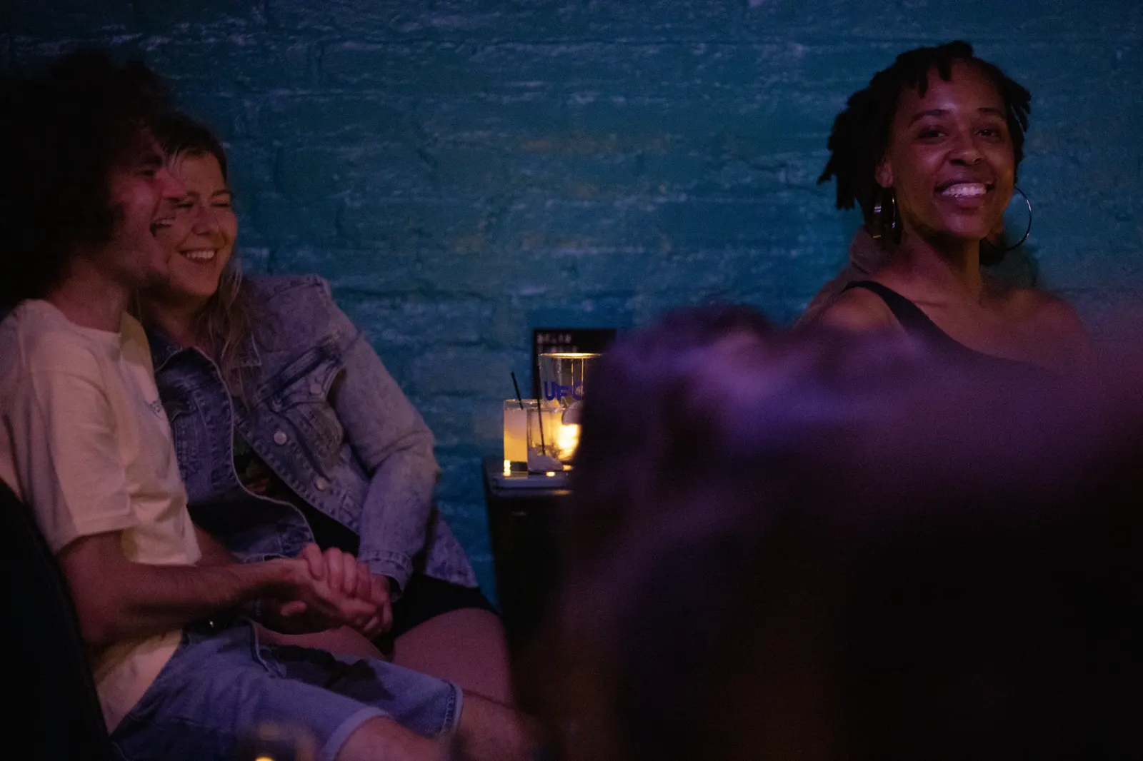 Audience laughing at candlelit tables against an exposed brick wall during a comedy show